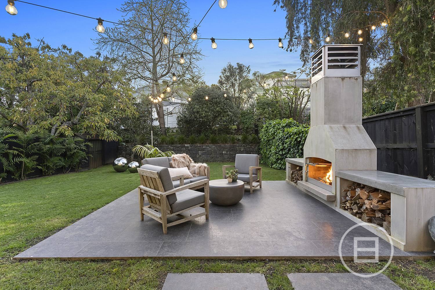 A lush central Auckland courtyard garden by Ponsonby Gardens, with festoon lights, established planting and an outdoor fireplace at dusk